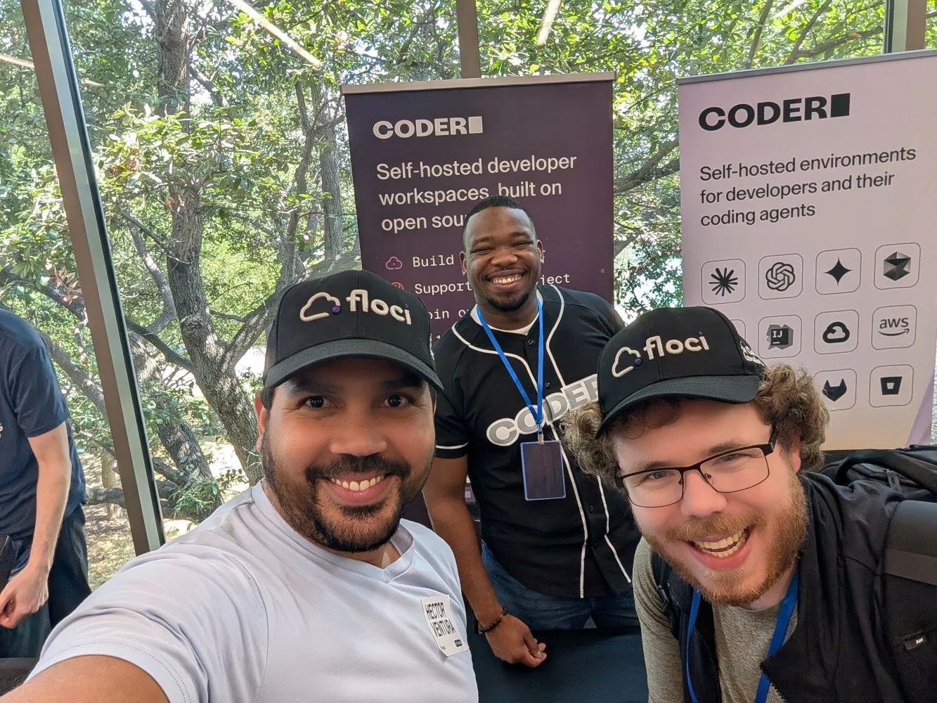 Three conference attendees posing at the Coder booth, two wearing Floci caps